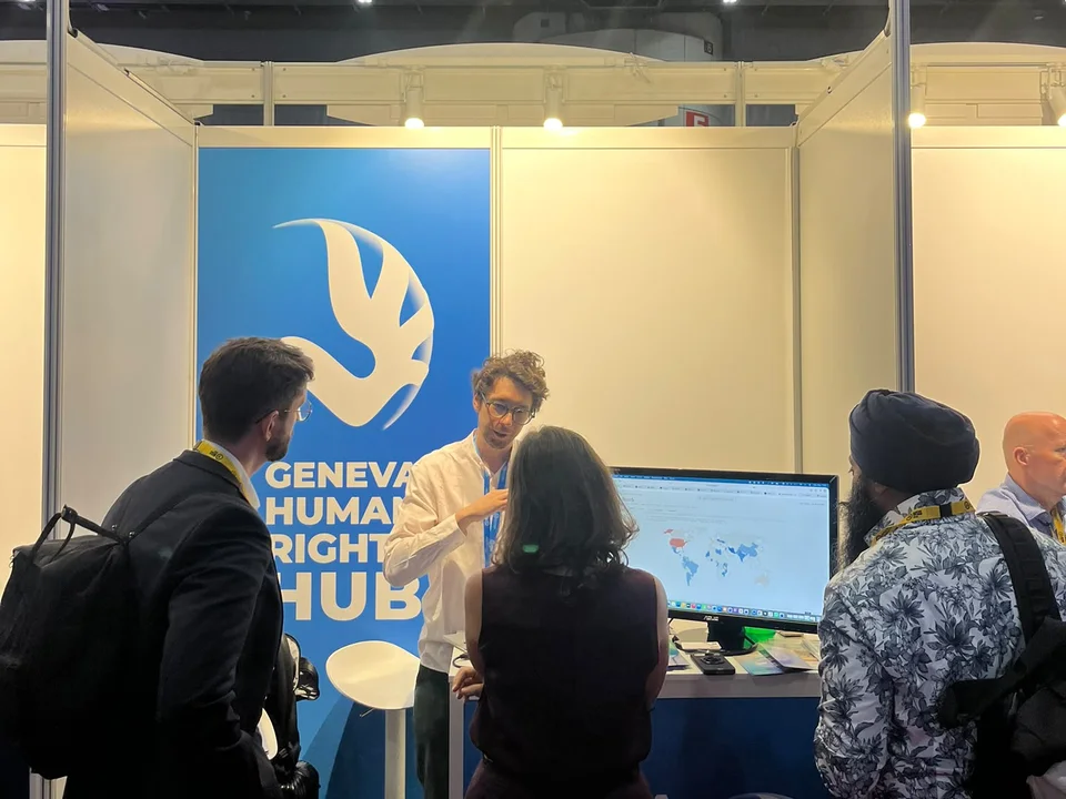 Łukasz Szoszkiewicz na stoisku Geneva Human Rights Hub pokazuje na monitorze mapę z HRC Voting