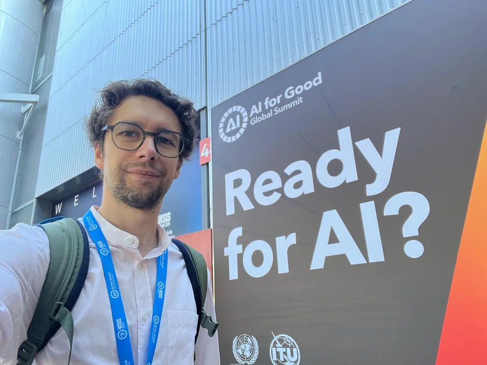 Łukasz Szoszkiewicz przed banerem Ready for AI? na AI for Good Global Summit w Genewie, lipiec 2026